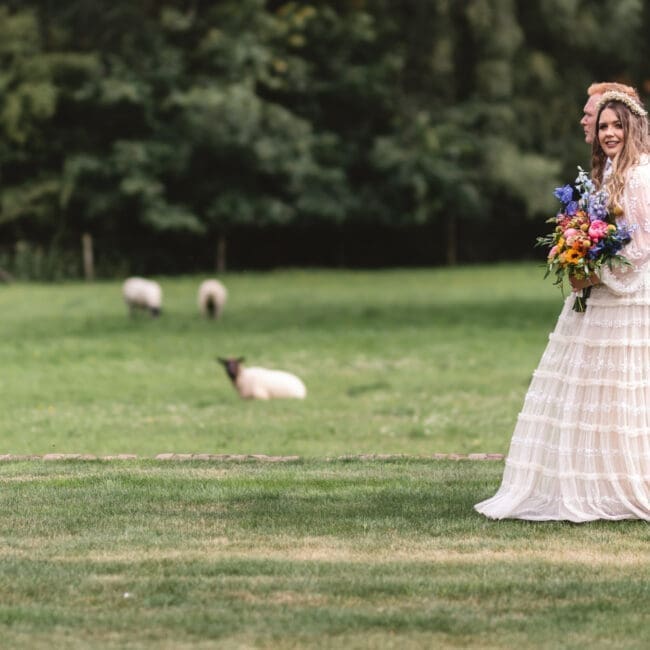 Marianne & Sam 15-07-2023 bride and groom walking at burtonfields hall york with sheep in the background