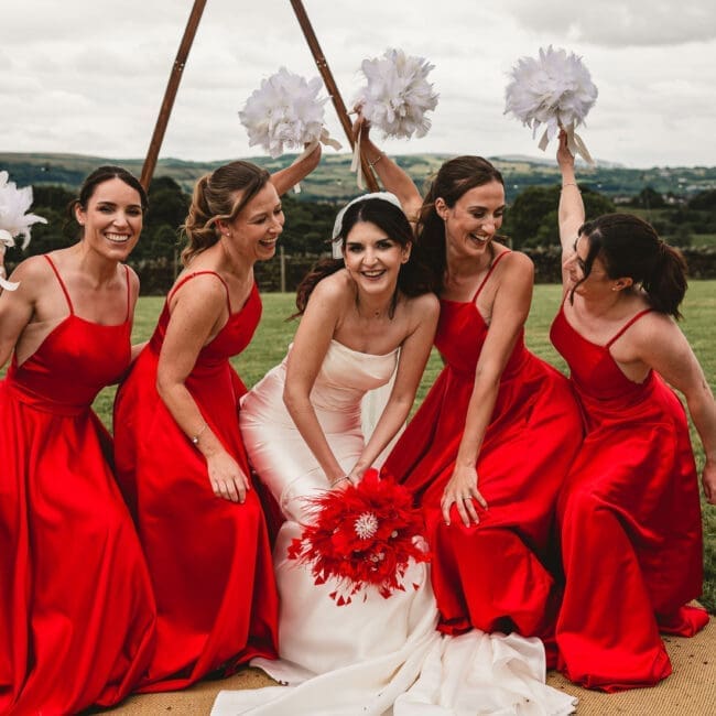 A75A3662-Edit Bridesmaids in red outfits ducking down at east riddlesden hall holding white feathers in the air || West Yorkshire Wedding Photographer