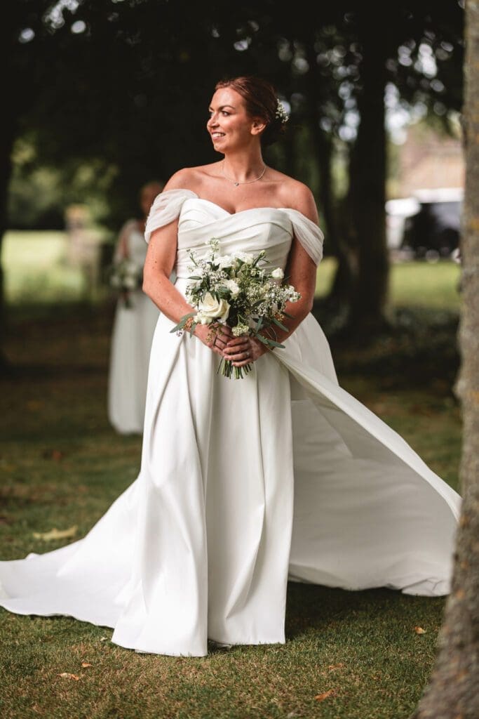 a bride holding her boquet with her dress flowing in the wind wth the beautiful sun on her face at the tithe barn bolton abbey