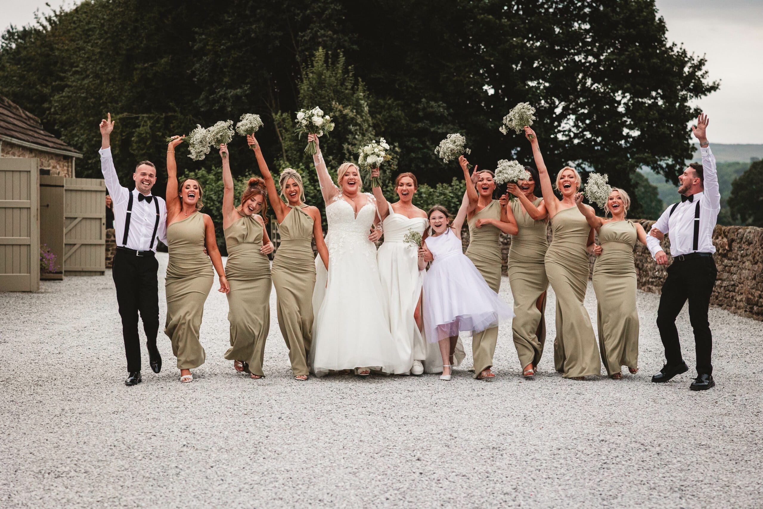 a full bridal party of bridesmiads, flowers girls and groosmen dressed in sage green bridesmaid dresses and flowers in the air walking as they enjoy there wedding at the tithe barn bolton abbey