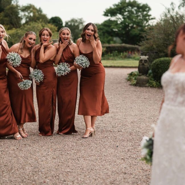 Jess & Alex – 1125 Bridesmiads dressed in bronze dresses looking in disbelieve at a beautiful bride at hodsock priory| Hodsock priory wedding photographer