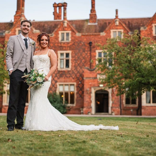 Jess & Alex – 1165 Bride and groom posing for a photo at hodsock priory with venue in the background | Hodsock priory wedding photographer