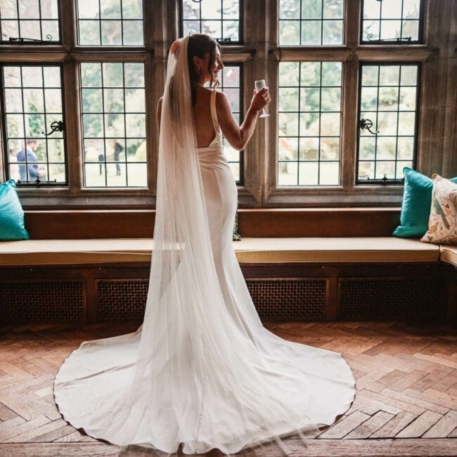 Ellie & sam – 2374 Bride in the window drinking prosecco at tissington hall | Tissington wedding photographer