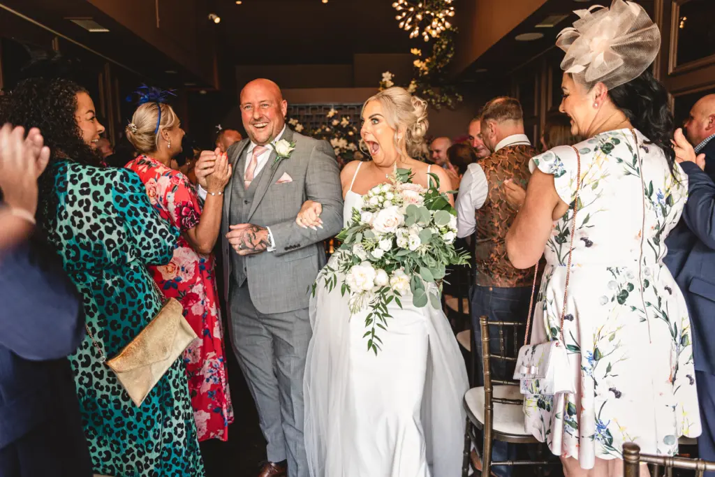 Liv and John laughing as guests cheer them back down the aisle at their Yorkshire wedding