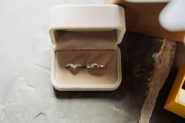 Two silver rings, one with small diamonds and one plain, displayed in an open beige ring box on a gray stone surface—perfect for a Yorkshire wedding or an elegant celebration at Oakwood at Ryther.