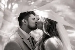 A bride and groom share a kiss under a flowing veil at Eyam Hall, with soft light and a blurred outdoor background, creating a romantic and dreamy weddings atmosphere.