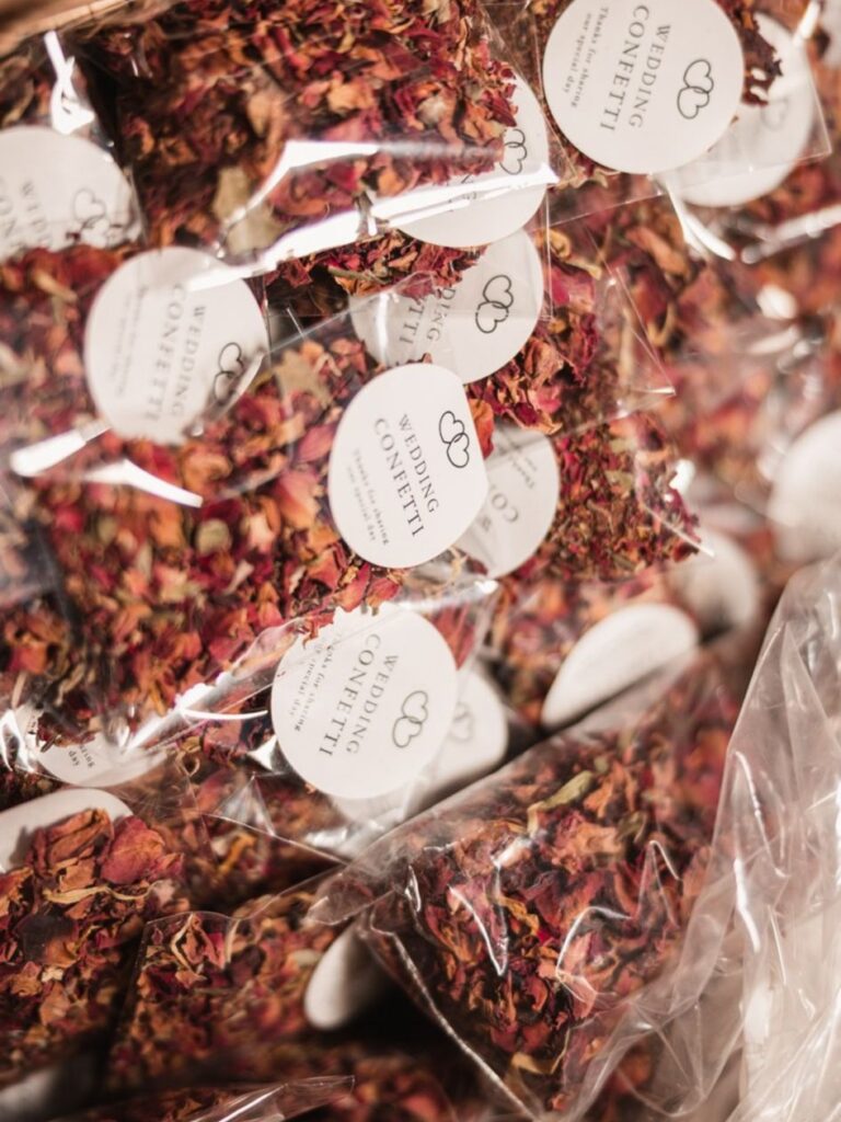 Several clear plastic bags filled with dried flower petals labeled Wedding Confetti are stacked together, ready for a celebration—showing what confetti best suits the perfect wedding.