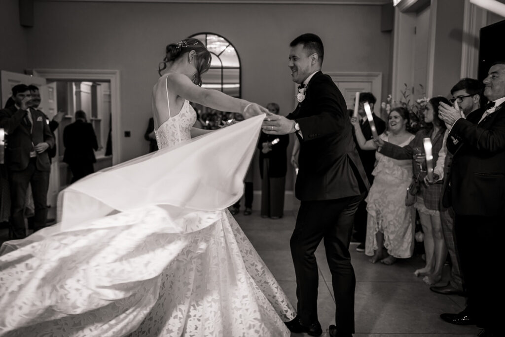 A bride and groom joyfully dance together at their Saltmarshe Hall wedding reception, surrounded by clapping and smiling guests. The bride’s dress flares as they spin, filling the scene with celebration and happiness.