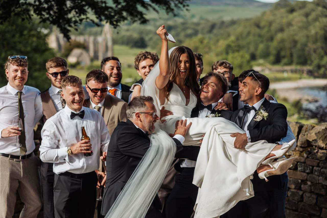 Chloe being lifted by the groomsmen, everyone laughing, at her Yorkshire wedding