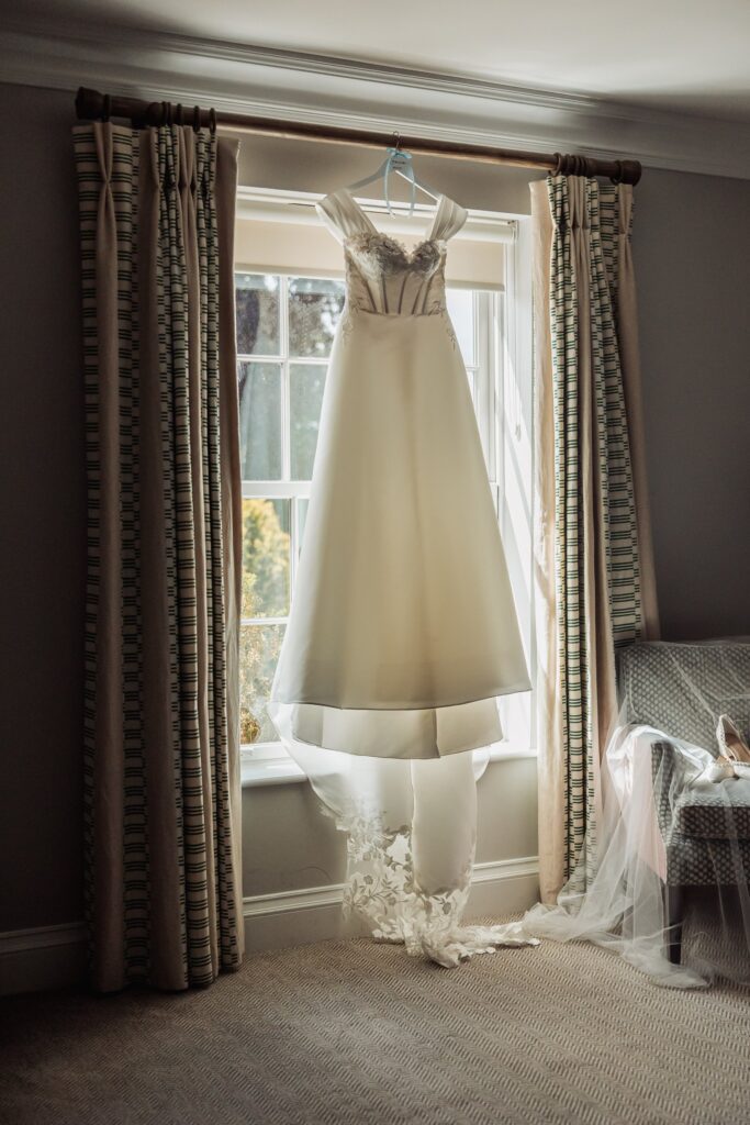 The wedding dress hangs at the bedroom window, its lace train pooling on the floor.