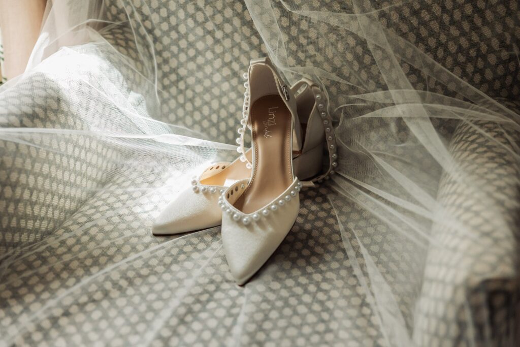 Pearl-trimmed bridal shoes resting on the veil before the ceremony.