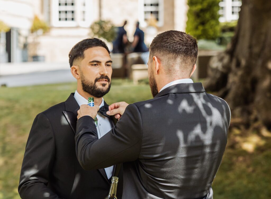 A groomsman adjusts the groom's bow tie in the grounds at Wentbridge House Hotel.