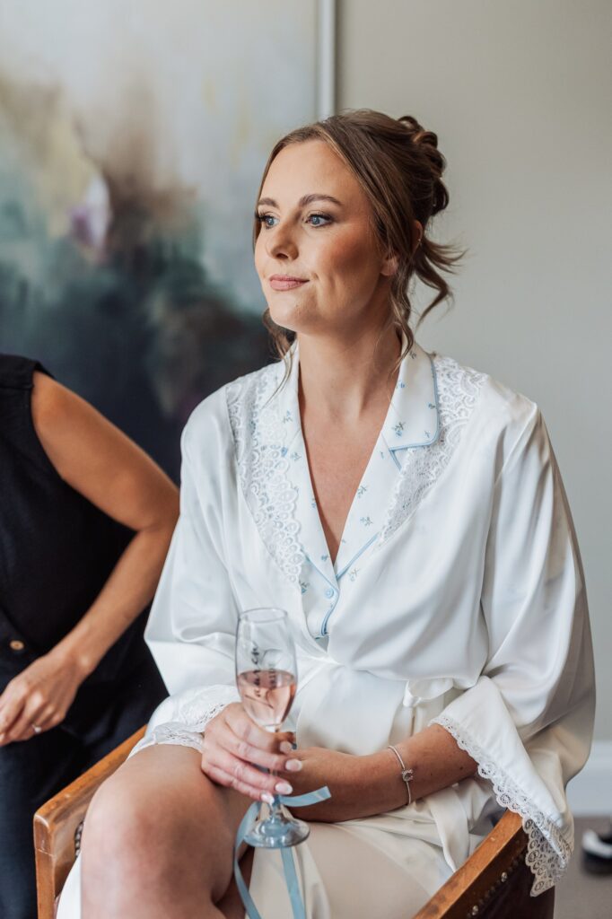 The bride pauses with a glass of champagne during bridal preparations.