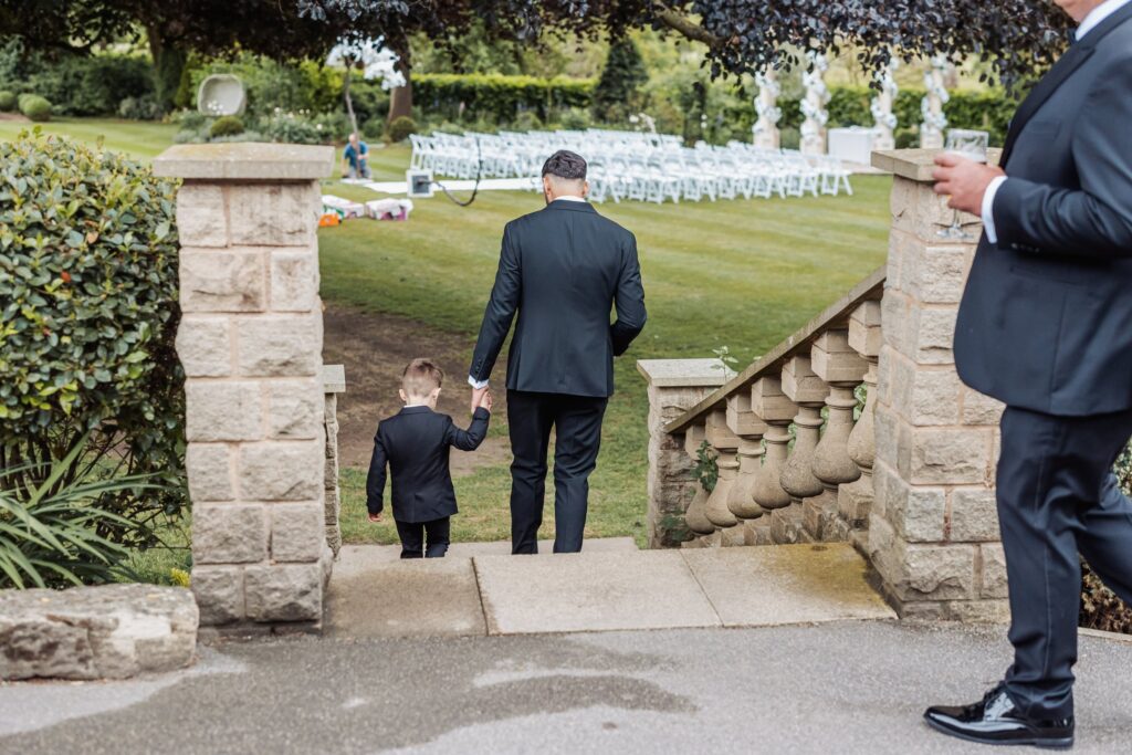 A guest walks the page boy down the stone steps towards the ceremony lawn at Wentbridge House Hotel.