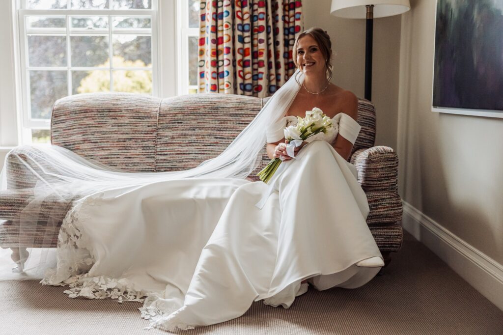 Bridal portrait on the sofa, veil spilling across the room, holding a calla lily bouquet.