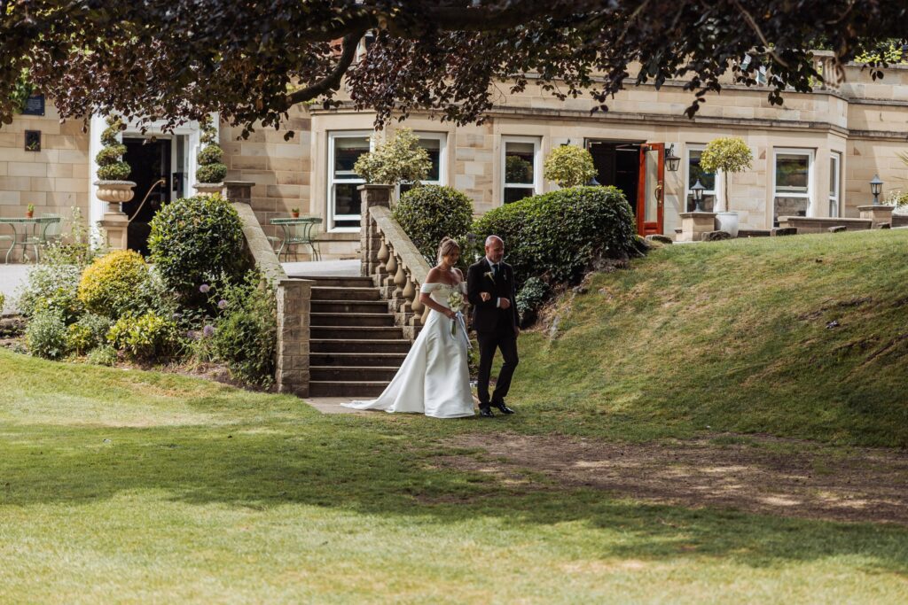 The bride and her father come down the stone steps from the house towards the ceremony lawn.