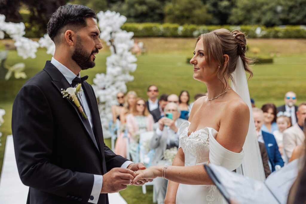 The groom places the ring on his bride's finger during their garden ceremony.