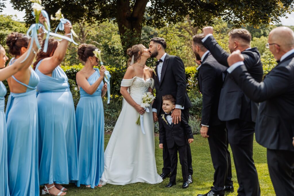 The bridal party cheer as the newlyweds kiss in the gardens at Wentbridge House Hotel.