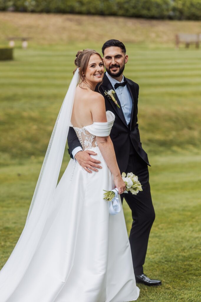 Bride and groom on the striped lawn at Wentbridge House Hotel, her cathedral veil trailing behind her.