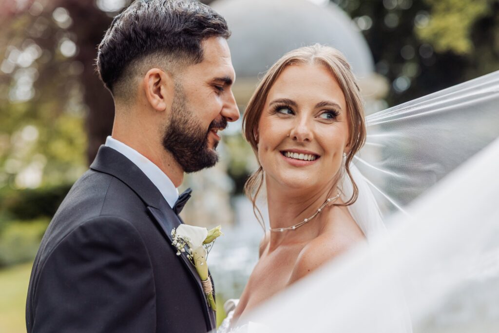 The bride looks up at her husband as her veil catches the breeze.