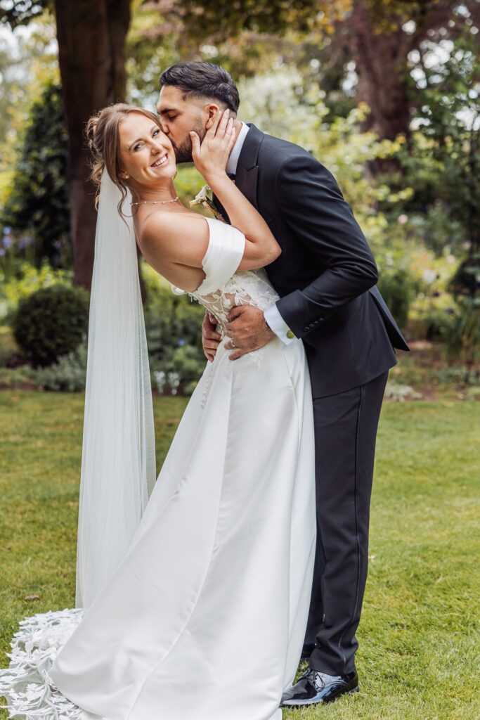 The groom kisses his bride's cheek in the formal gardens at Wentbridge House Hotel.