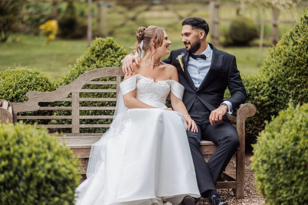 Bride and groom sit together on a bench in the formal gardens at Wentbridge House Hotel.