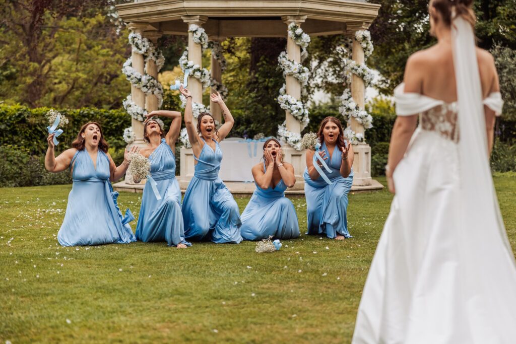 The bridesmaids drop to their knees cheering as the bride walks towards them.