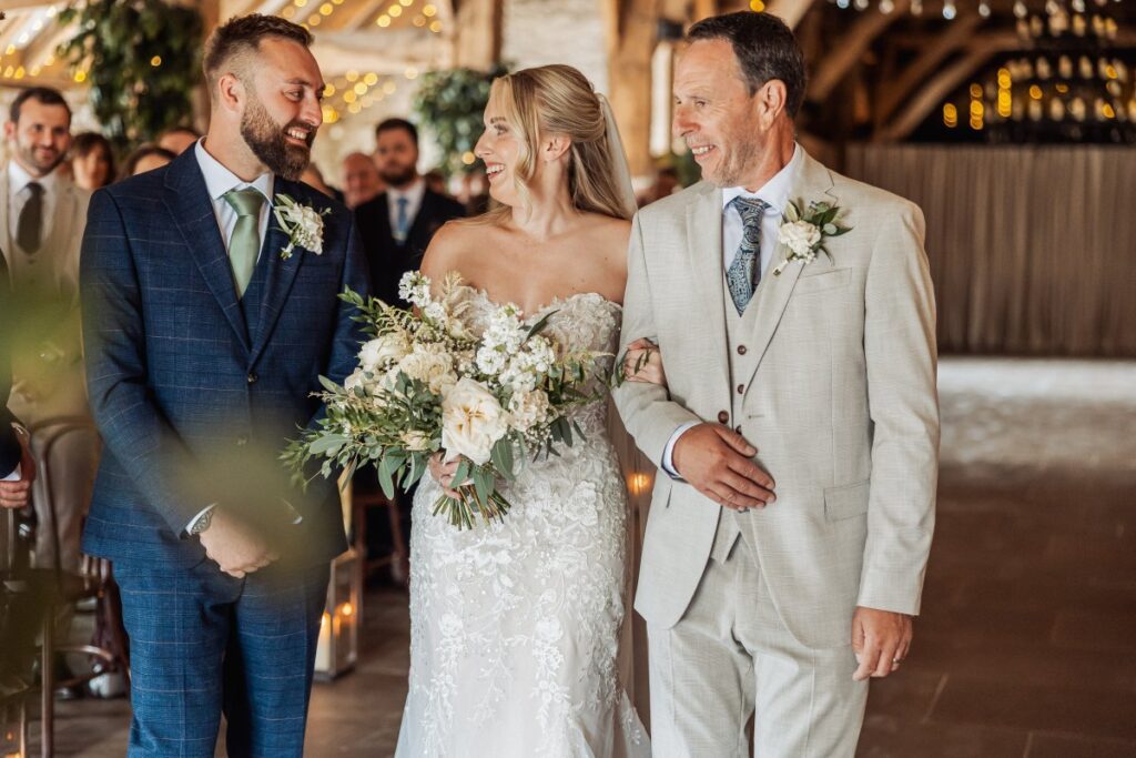 The bride reaches the front of the ceremony with her father and the groom at Tithe Barn Bolton Abbey.