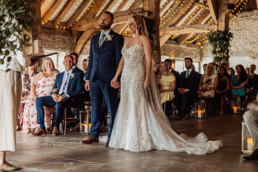 Bride and groom stand together during their ceremony at Tithe Barn Bolton Abbey, guests seated beneath the fairy-lit beams.