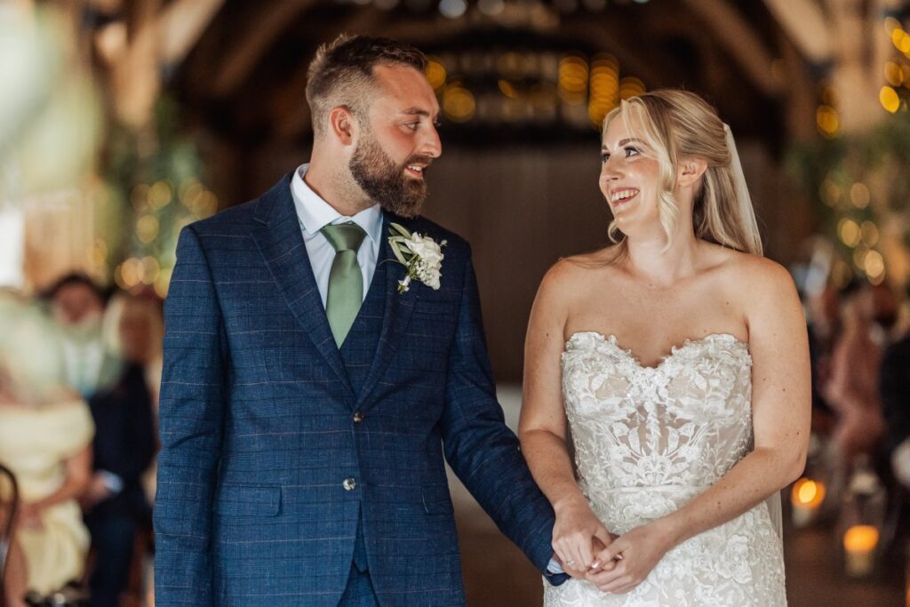 Bride and groom hold hands during their ceremony at Tithe Barn Bolton Abbey, guests seated behind them.