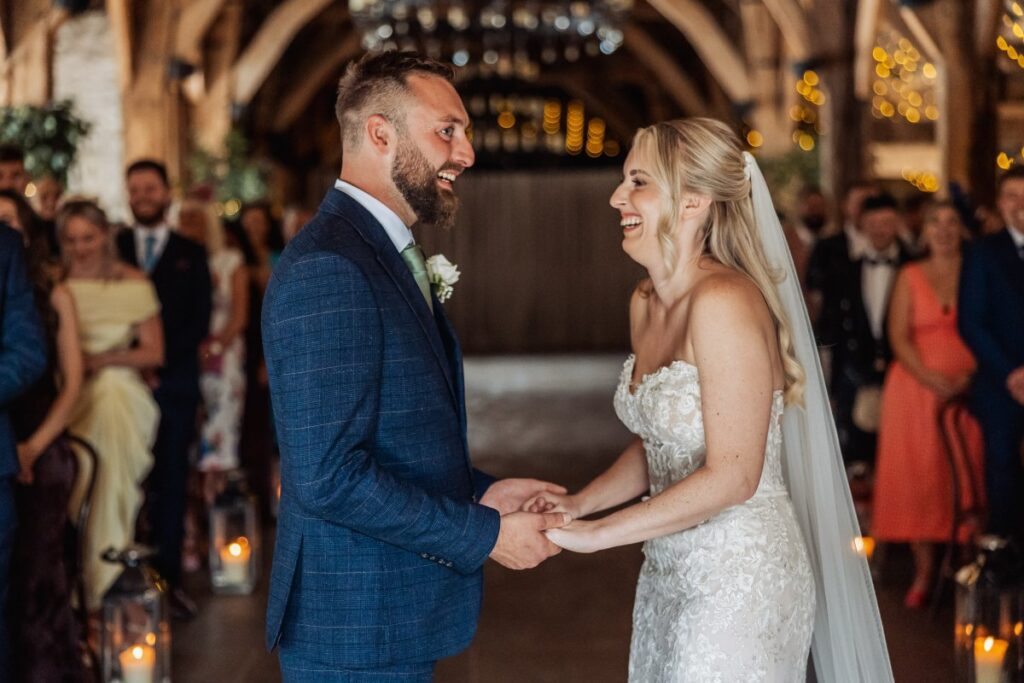 The couple laugh together as they exchange vows at Tithe Barn Bolton Abbey, candle lanterns lining the aisle.