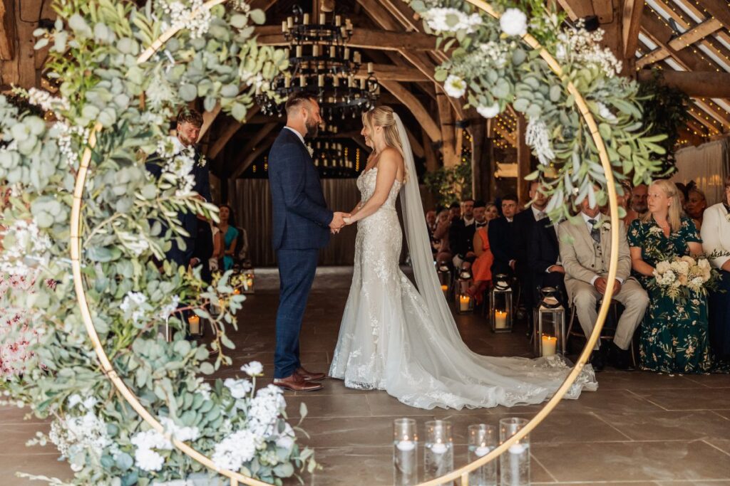 Bride and groom exchange vows beneath a circular floral arch of eucalyptus and white blooms at Tithe Barn Bolton Abbey.