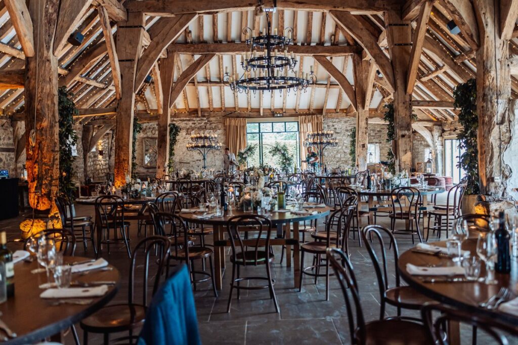The main barn at Tithe Barn Bolton Abbey laid for the wedding breakfast, round tables beneath the iron chandeliers.