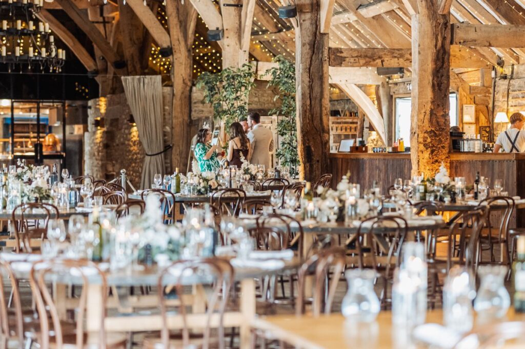 Tables set for the wedding breakfast at Tithe Barn Bolton Abbey, with the bar and foliage-wrapped posts behind.