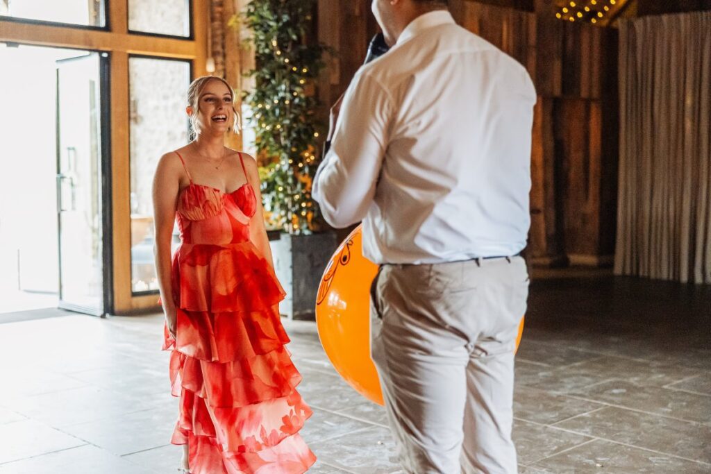 The bride in a vibrant red ruffled gown dances with her groom in a crisp white shirt and beige trousers, surrounded by warm wooden paneling and festive lights at Tithe Barn, Skipton