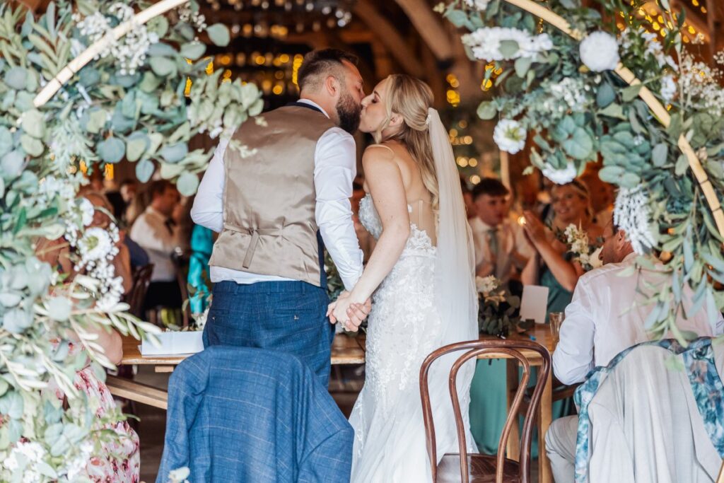 The couple kiss beneath the eucalyptus arch at the top table at Tithe Barn Bolton Abbey.