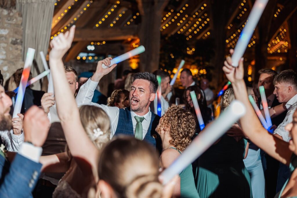 Guests wave glow sticks in a lively first dance, illuminated by warm marquee lights and festive string decor at Tithe Barn, Skipton