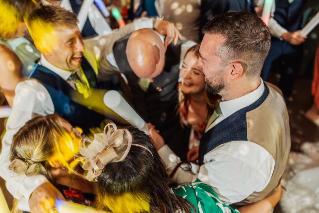 The confetti exit bursts with joy as the bride, in a vibrant yellow dress, and groom, in a tan suit, hold hands, surrounded by cheering guests and a child in a red outfit at Tithe Barn, Skipton