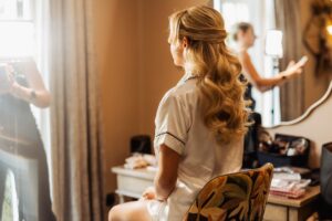 A woman with long, wavy blonde hair is seated in a dressing room, preparing for a wedding at Woodlands Hotel, Leeds
