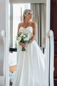 A woman in a strapless white wedding dress holds a bouquet of white flowers and greenery at Woodlands Hotel, Leeds