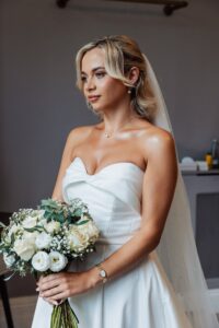 A woman in a white strapless wedding dress holds a bouquet of white flowers and greenery at Woodlands Hotel, Leeds