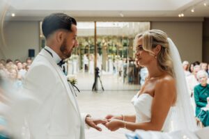 A couple exchanging rings during a wedding ceremony, with guests seated in rows behind them