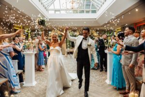 A couple in wedding attire walks through a room filled with guests throwing confetti, creating a joyful and celebratory atmosphere