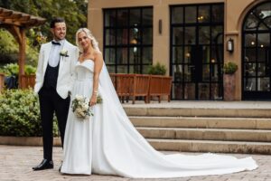 A couple in wedding attire stands on a stone staircase, the bride in a strapless white gown with a long veil and holding a bouquet at Woodlands Hotel, Leeds
