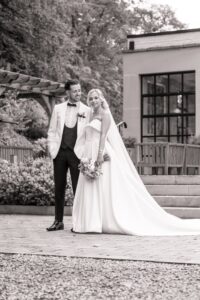 A couple in wedding attire stands together on a stone pathway, with the bride holding a bouquet and the groom in a white tuxedo at Woodlands Hotel, Leeds
