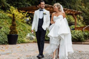 A couple in wedding attire walks together outdoors, smiling and holding hands at Woodlands Hotel, Leeds