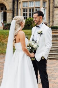 A couple in wedding attire stands close together, smiling at each other at Woodlands Hotel, Leeds