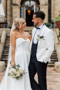 A couple in wedding attire stands close together, smiling at each other at Woodlands Hotel, Leeds