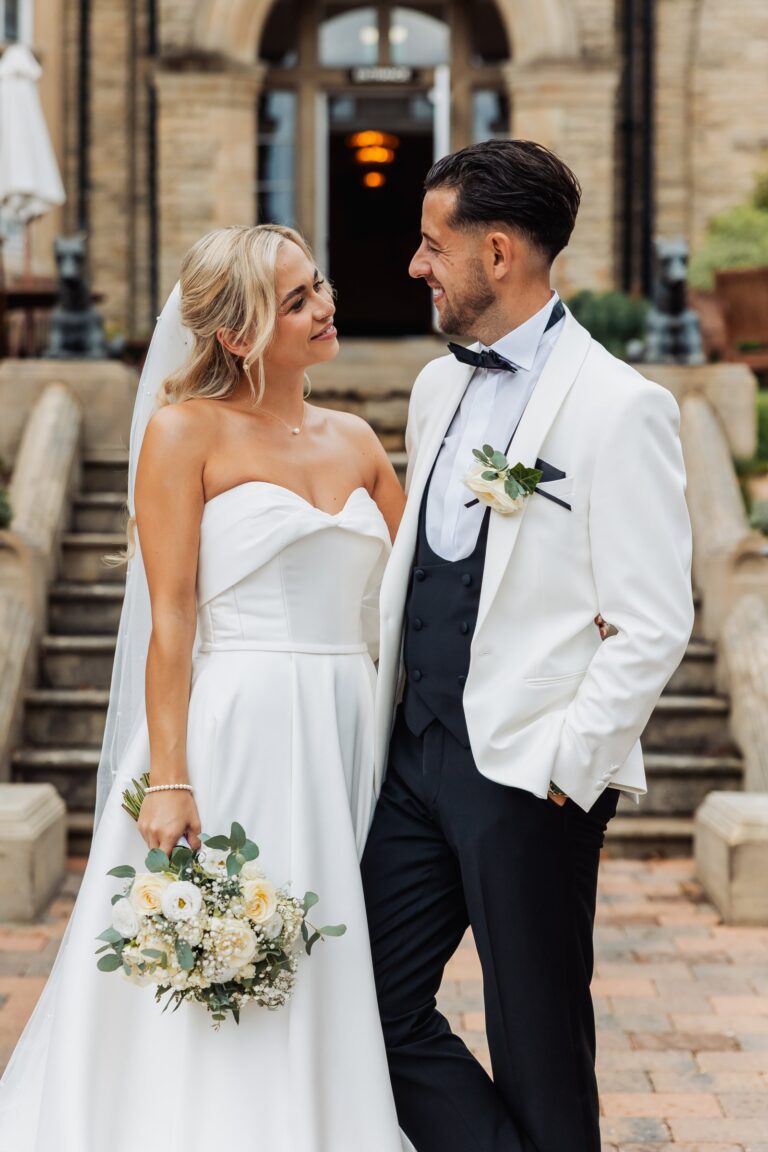 A couple in wedding attire stands close together, smiling at each other at Woodlands Hotel, Leeds