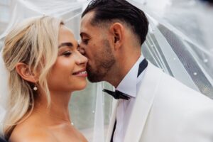 A couple in wedding attire share a tender moment beneath a sheer white veil, with the woman wearing a pearl necklace and earrings at Woodlands Hotel, Leeds